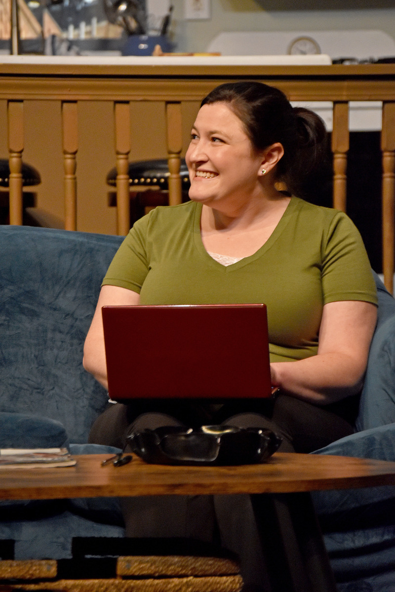His friend grins over her laptop on the couch.