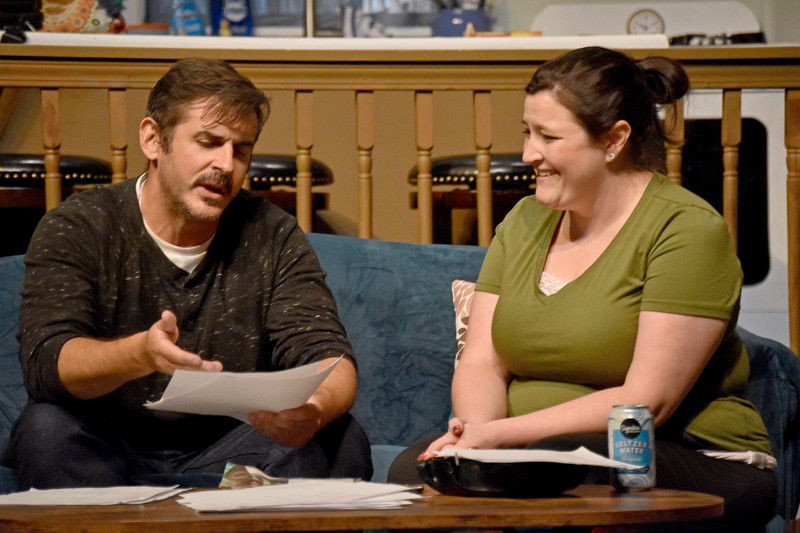 He holds up a printout; she laughs.