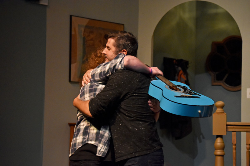 His roommate, guitar on his back, pulls him into a hug.