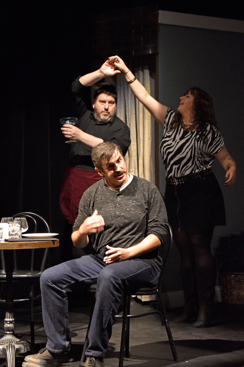 Two dancers behind him as he sits at the table.