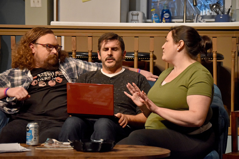 Three friends crowd the couch around a laptop; she argues her point.