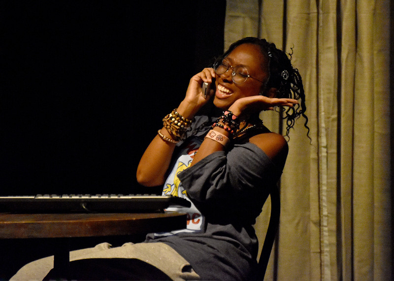 On the phone at her keyboard, she laughs, hand to her head.