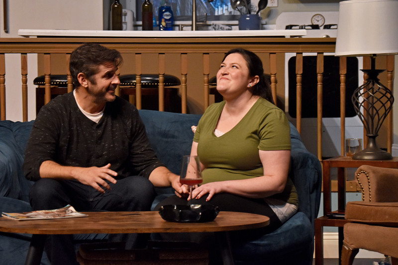 On the couch, she grins upward as he smiles at her.
